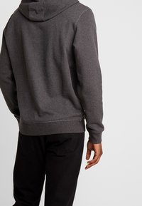 Szara bluza z kapturem z ryflowanymi mankietami i dołem. Wykonana z miękkiego, polaru, z kontrastowymi szwami na brzegach. Stylizowana w luźnym fasonie.
