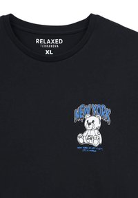 T-shirt nera in cotone con grafica di un orso cartone e il testo blu "NEW YORK" e la frase "NEW YORK NON È UNA CITTÀ, È UN MONDO."
