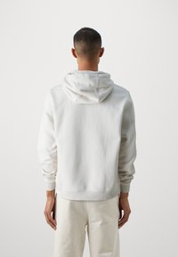 Ljusgrå hoodie av mjukt material. Har en huva, ribbade ärmslut och en avslappnad passform. Slät textur med minimal synlig sömnad.