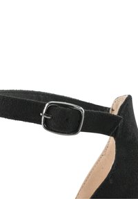 Musta nilkkaremmi kenkä, jossa on teksturoitu mokkajäljitelmä, varustettuna metallisella soljella säätämistä varten ja kapealla korko-ominaisuudella.