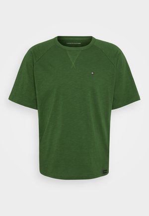 Camiseta verde de manga corta con cuello redondo, fabricada con tela suave. Presenta un detalle de costura tonal y un pequeño logotipo en el pecho izquierdo.