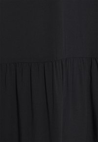 Abito nero con un design a strati e texture arricciate in vita. Realizzato in un tessuto liscio con una leggera lucentezza.
