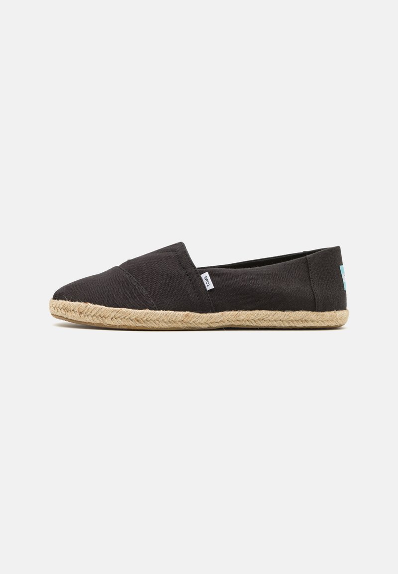 Chaussure noire à enfiler en toile avec une semelle en jute et des détails cousus. Présente une petite étiquette sur le côté.