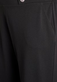 Melnas bikses ar gludu tekstūru, kurām priekšpusē ir kabata un sudrabota pogas detaļa pie vidukļa. Šūtas pēc pasūtījuma, bez rakstiem.