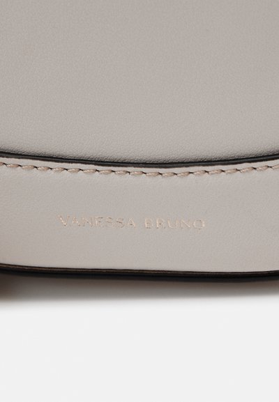 Light gray leather bag detail featuring embossed "VANESSA BRUNO" logo, contrasting black edge stitching, smooth texture, and minimalist design.