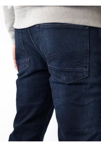 Jeans de mezclilla azul oscuro con un diseño ajustado, que cuentan con dos bolsillos traseros y detalles de costura sutiles. La tela parece suave.