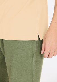 Vaaleanbeige lyhythihainen paita, jossa on sivurei'ät, yhdistettynä vihreisiin teksturoituihin housuihin, jotka esittelevät rentoa istuvuutta ja epämuodollista muotoilua.