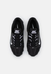 Zapatillas de entrenamiento negras con parte superior de malla, acentos blancos y suela estructurada. Presenta cordones y un collar acolchado para mayor comodidad. Logotipo de Nike visible.