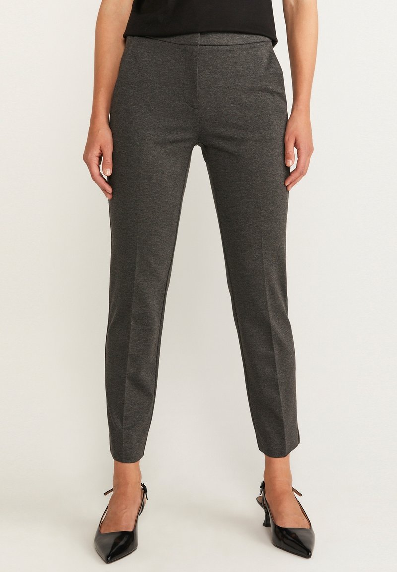 Pantalon gris ajusté avec une coupe slim, présentant une texture lisse et un pli avant. Porté avec des escarpins noirs pointus pour un contraste.
