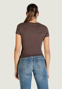 Hnědé přiléhavé tričko s krátkými rukávy, doplněné světlými modrými džínami s klasickým pětiprůstkovým designem a vybledlými detaily.