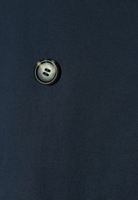 Tessuto blu navy con un bottone rotondo metallico con due fessure orizzontali. Tessuto liscio con un design semplice ed elegante.