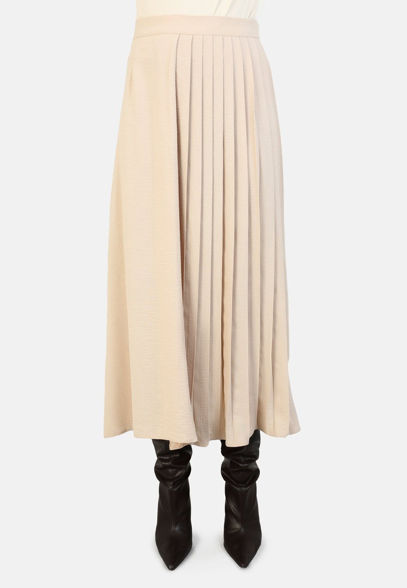 Beige pleated skirt, valmistettu kevyestä kankaasta, joka on sileä tekstuuriltaan ja jossa on tiukka vyötärö, yhdistettynä korkeisiin mustiin korkokenkiin.