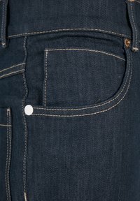 Jeans in denim scuro con una tasca laterale distintiva, cuciture beige a contrasto e dettaglio in metallo bianco sul bottone.