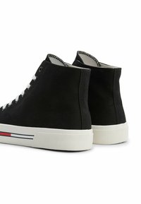 Zapatillas altas negras de lona, con cordones blancos, suela blanca y detalles de rayas rojas y azules en la parte inferior.