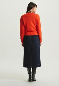 Un pull en tricot orange avec un ourlet et des poignets côtelés, associé à une longue jupe en denim foncé avec des coutures visibles, et des bottes noires jusqu'aux genoux.