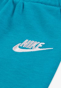 Türkiisi värvi kangas pehme tekstuuriga, millel on valge tikitud Nike'i logo. Kujundus sisaldab lihtsat, klassikalist ovaalset kuju.