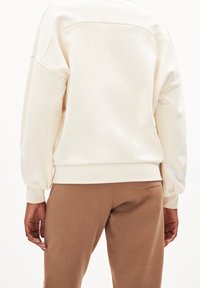 Felpa color crema con un fit rilassato, spalle scese e polsini a costine, abbinata a pantaloni della tuta marroni. Tessuto morbido e liscio.