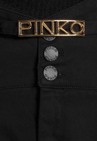 Tissu en denim noir avec trois boutons noirs embossés "PINKO" et une plaque logo métallique rectangulaire dorée "PINKO" au-dessus.