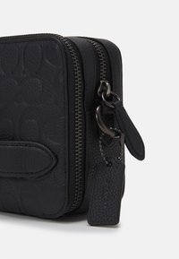 Portafoglio in pelle nera con texture a grana, dotato di chiusura a zip, etichetta con logo e un motivo in rilievo di forme intrecciate.