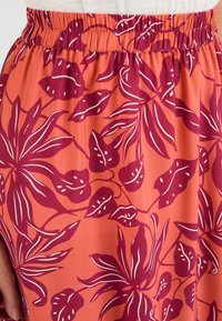 Bloemenrok met een elastische taille. Kenmerkt zich door een roze-oranje achtergrond met grote kastanjebruine en witte bladdessins. Zachte, vloeiende stof.