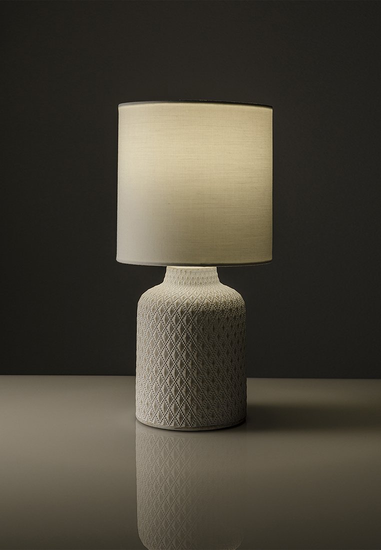 Keramická lampa s texturovaným, diamantovým vzorem na základně ve světle béžové barvě, zakončená cylindrickým bílým textilním stínidlem, které vrhá jemné světlo.