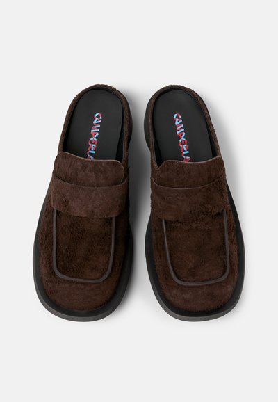 Pantofole marroni slip-on con tomaia in tessuto texture, cinturino rettangolare e suole in gomma nera. Presentano un vivace logo del marchio sulla soletta.