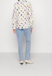 Camisa de manga larga con cuello y patrones abstractos multicolores sobre un fondo claro, combinada con vaqueros azul claro y botines texturizados beige.