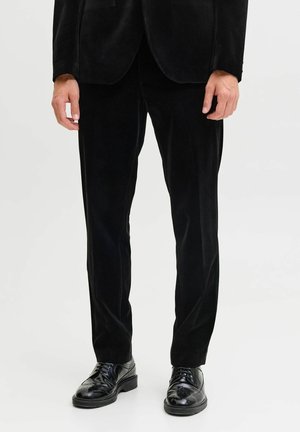 Pantalons de costume en velours noir avec une coupe slim, associés à des chaussures de ville noires élégantes avec des détails en brogue et des lacets lisses.