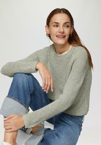 Hellgrauer gestrickter Pullover mit geripptem Muster und Rundhalsausschnitt, kombiniert mit faded blauen Jeans, die hochgekrempelte Säume haben.