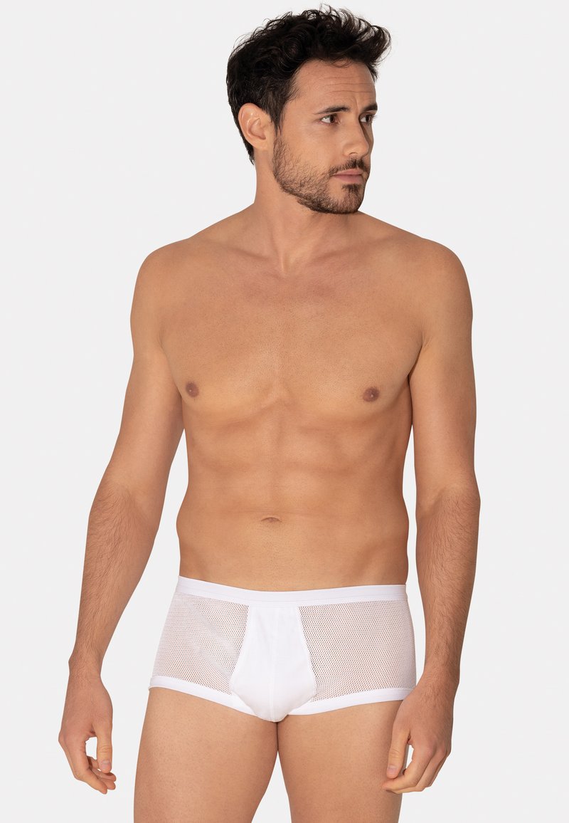 Slip en maille blanche avec ceinture solide, dotée d'une poche à l'avant et d'un design ajusté. Le tissu a une texture transparente et respirante.