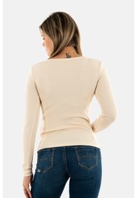 Top beige a maniche lunghe a coste con scollatura tonda, abbinato a jeans in denim blu scuro con tasche posteriori e dettagli di cucitura sottili.