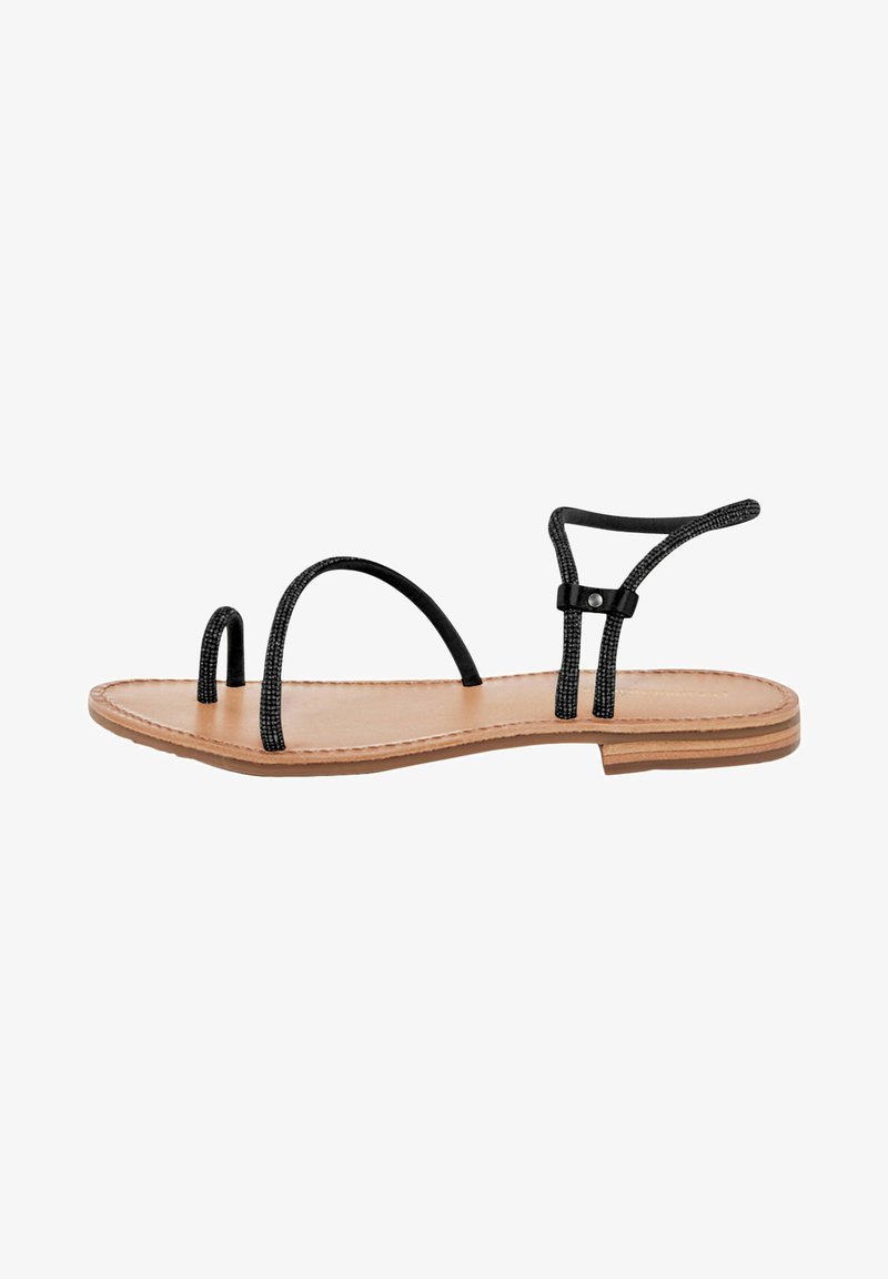 Sort ankelrem sandal med tynde sorte remme, flad lys brun sål, minimalistisk design og dekorativ syning langs kanterne.