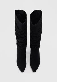Bottes noires montantes en daim doux, avec un design froncé, un bout pointu et un intérieur lisse. Semelles plates pour le confort.