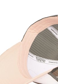 Vue intérieure d'une casquette de baseball beige montrant la doublure intérieure cousue, un panneau en maille et une étiquette de marque indiquant "Von Dutch" et "California".