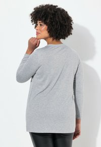 Haut gris à manches longues avec un col rond, texture douce et coupe décontractée. Présente la vue de dos, associé à un pantalon noir en simili-cuir.