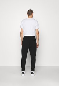 Svarta sweatpants med en figurnära silhuett, muddar i benen och en bakficka. Bärs tillsammans med en enkel vit t-shirt och vita sneakers.