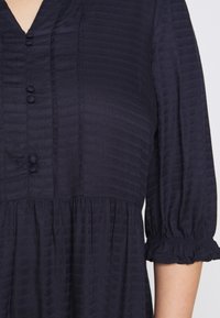 Vestido texturizado azul marino con rayas verticales, detalles de botones y mangas abullonadas. Cuenta con una cintura fruncida para un ajuste relajado.