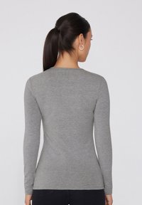 Langärmeliges Oberteil in Melange-Grau, aus weichem, leichtem Stoff gefertigt. Verfügt über einen Rundhalsausschnitt und eine taillierte Silhouette ohne Verzierungen.