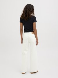 Calças de ganga brancas de perna larga com bolsos traseiros, apresentando um remendo de pele castanha na cintura. Combinadas com uma t-shirt preta justa.