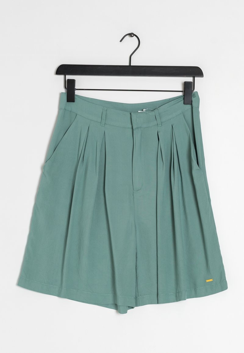 Shorts taille haute plissés couleur sarcelle avec passants de ceinture et poches latérales suspendus sur un cintre noir sur fond blanc.