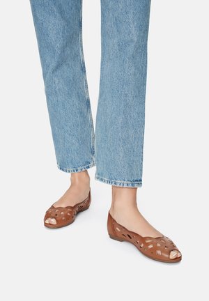 Braune offene Ballerinas aus gewebtem synthetischem Material, mit flachem Absatz, Cut-out-Design und glatter Oberfläche. Getragen zu hellblauen Jeans.