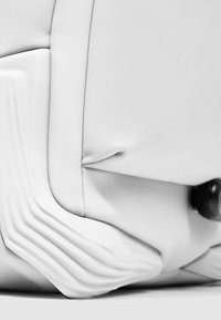 Witte synthetische tas met een gladde textuur, voorzien van gebogen lijnen en subtiele plooien. Heeft een zwart metalen accent voor de sluiting.