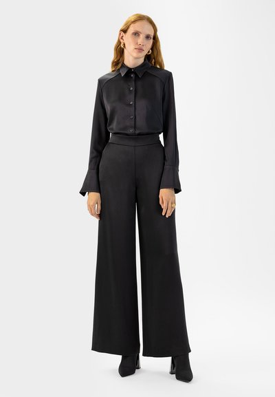 Zwarte zijden shirt met een puntige kraag en knoopsluiting, gecombineerd met zwart, hoge taille wijde broek, voorzien van lange klokmouwen.