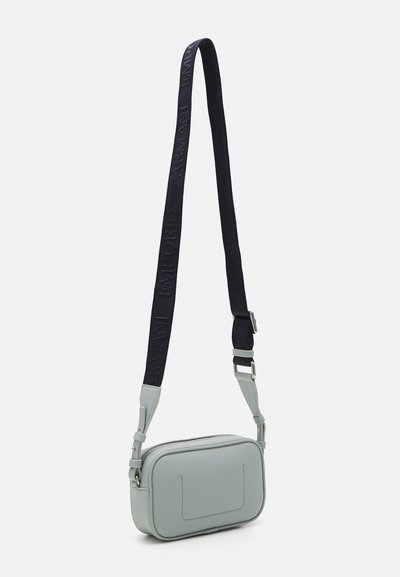 Borsa a tracolla in pelle verde chiaro con forma rettangolare, superficie testurizzata e tracolla blu scuro con testo del logo impresso. Chiusura a zip.