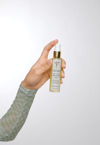 Bottiglia di olio leggendario Rahua dell'Amazzonia, trasparente con accenti dorati, forma circolare, 47 ml, etichettata per la cura dei capelli, tenuta contro uno sfondo bianco.