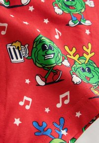 Červená látka so hravými zelenými rozprávkovými zeleninami s rukami, ktoré držia pivo, majú parohy a sú obklopené hudobnými notami a hviezdami.