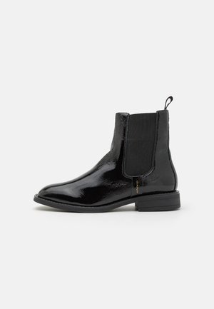 Schwarze Lackleder-Stiefelette mit spitzer Zehe, elastischen Seiteneinsätzen und einer kleinen Schlaufe an der Ferse. Flache, strukturierte Sohle.