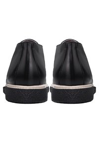 Paire de chaussures en cuir noir vues de dos avec des semelles noires texturées et des semelles intermédiaires blanches sur un fond blanc.