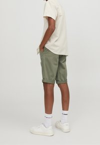 Lichtbeige kortearm shirt, olijfgroene opgerolde shorts, gecombineerd met witte sneakers en zichtbare witte sokken. Minimalistisch ontwerp, casual pasvorm.