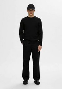 Camisola preta de mangas compridas, calças pretas e um boné preto. O conjunto apresenta um design simples com textura suave; sapatos com detalhes decorativos.